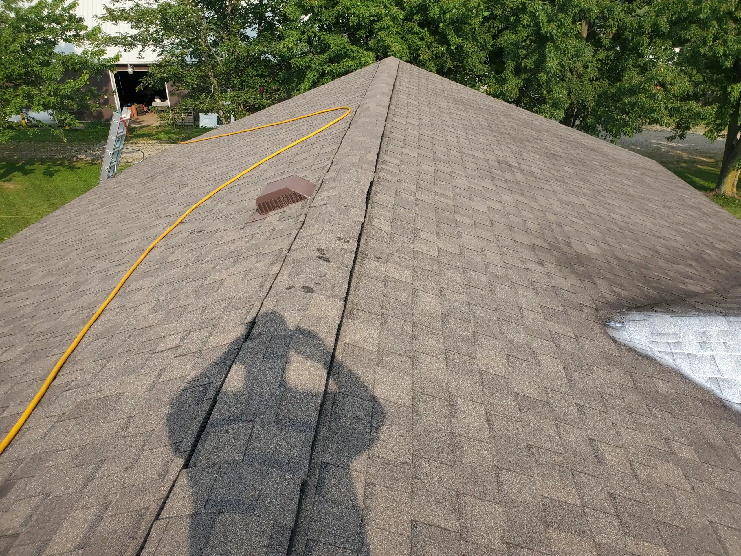 Person’s shadow on Gashill farmhouse roof with vent, yellow cable, and damaged area near silver patch.