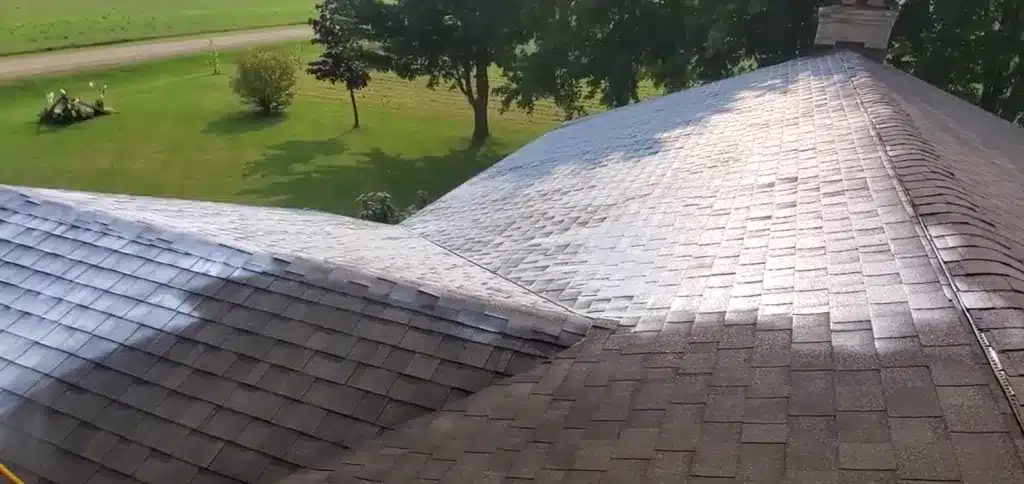 Partially cleaned farmhouse roof shingles overlooking green lawn and Gashill trees.