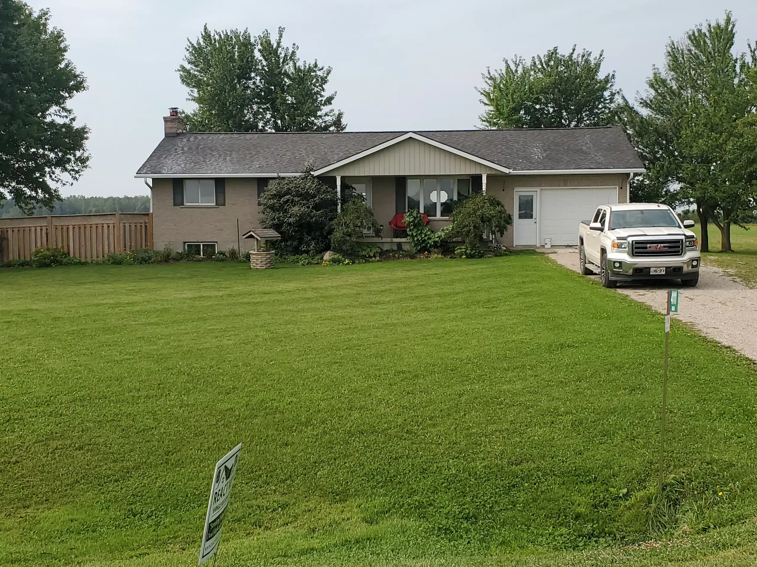 Single-story farmhouse with gravel driveway, white truck, and expansive green lawn.