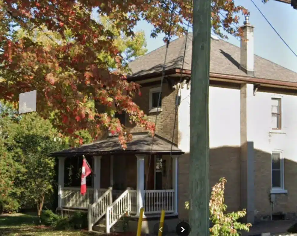 Milverton Ontario two-story house with shingle roof, front porch, Canadian flag, autumn tree.