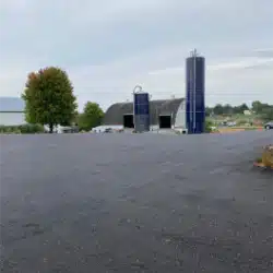 New Project (4) Paved lot with two silos and a barn beneath a cloudy sky.