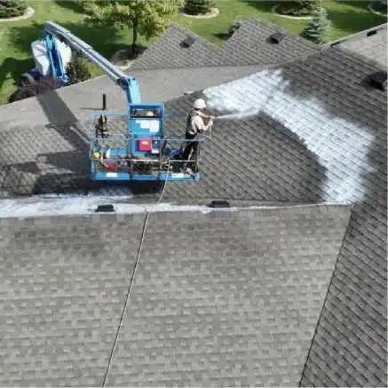 Worker on lift spraying white coating onto sloped shingle roof in Victoria BC.
