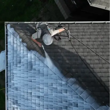 Worker in safety gear pressure washing roof shingles above DC Baltimore car dealership.