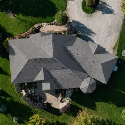 after-im-400×400 House with gray roof, green lawn, trees, and gravel driveway seen from above.