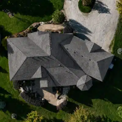 before-im-400×400 Large house with gray roof, green lawn, and gravel driveway seen from above.