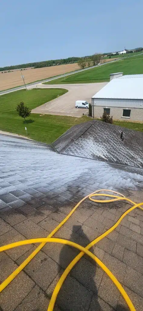 Yellow hose on shingled roof with white cleaning solution and visible shingle loss near Donegal, Ontario.