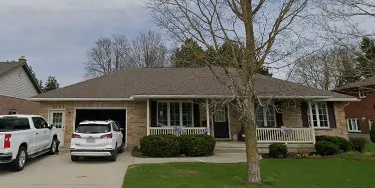 Single-story brick bungalow with two cars in the driveway, tree in yard, shingles look refreshed.