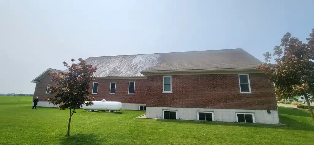 Brick building, white propane tanks, small tree, and missing shingles on a patchy roof outside.