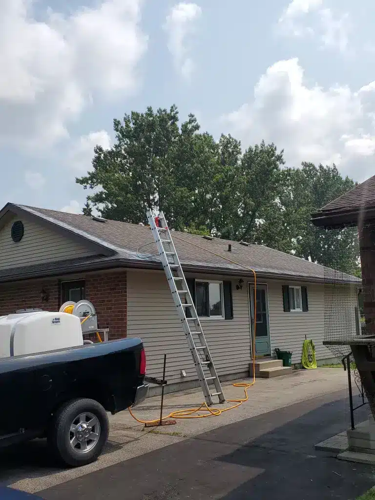 Ladder leaning on asphalt shingle roof of house in Palmerston, Ontario, with cloudy sky above.