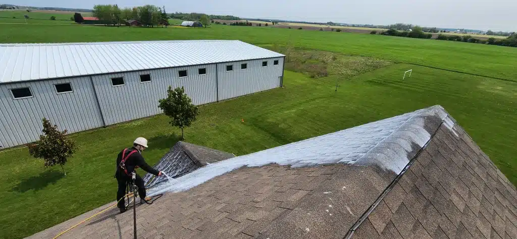 Worker in safety gear applies protective white coating to church roof in Donegal, Ontario.