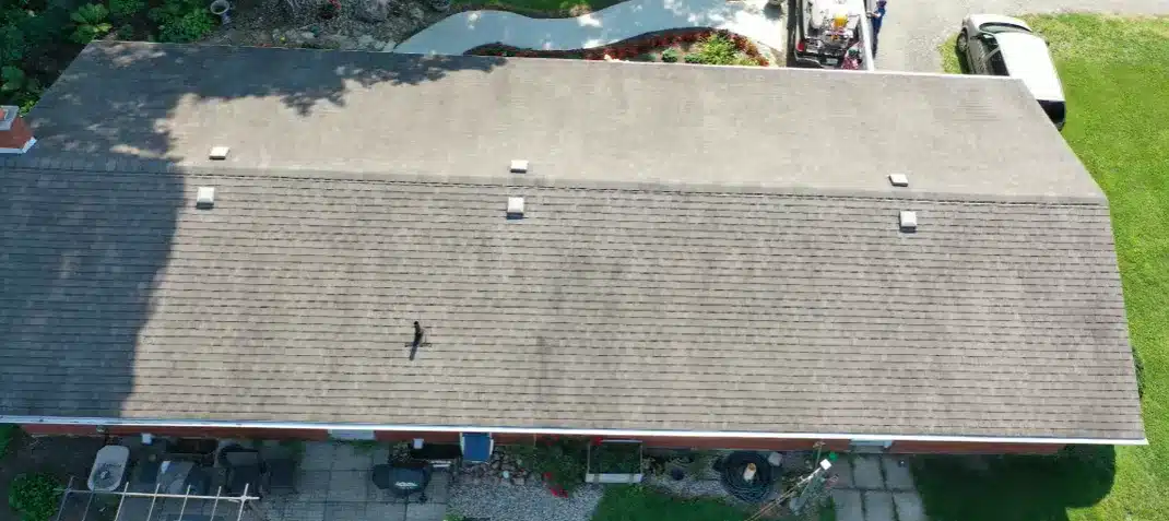 Aerial view of asphalt shingle roof with vents, partial shadow, and adjacent grassy yards.