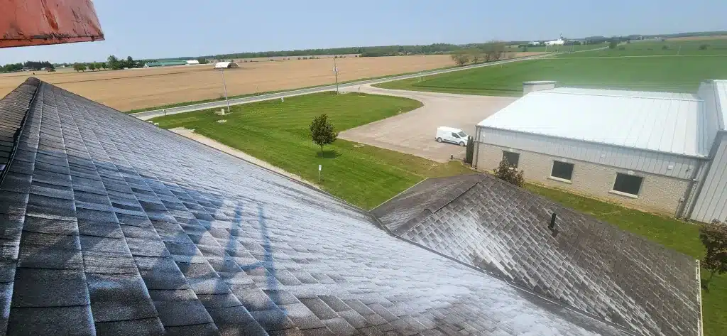 Sloped roof in Donegal Ontario with distant fields and visible shingle loss on a nearby building.